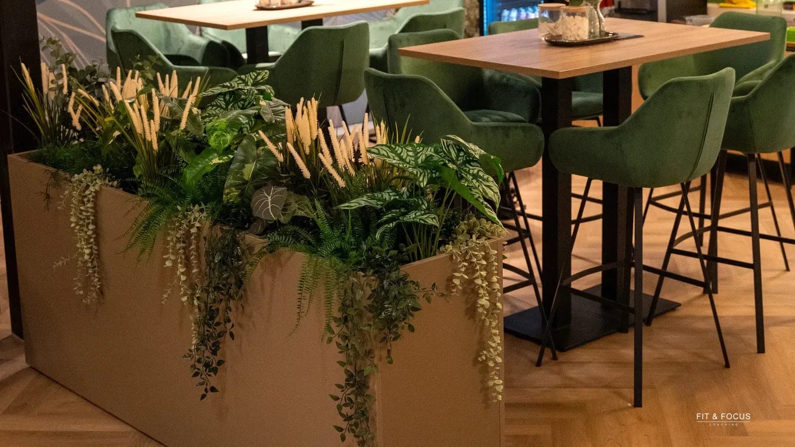 Zithoek met hoge tafels en groene stoelen bij de plantenbak in de zaak
