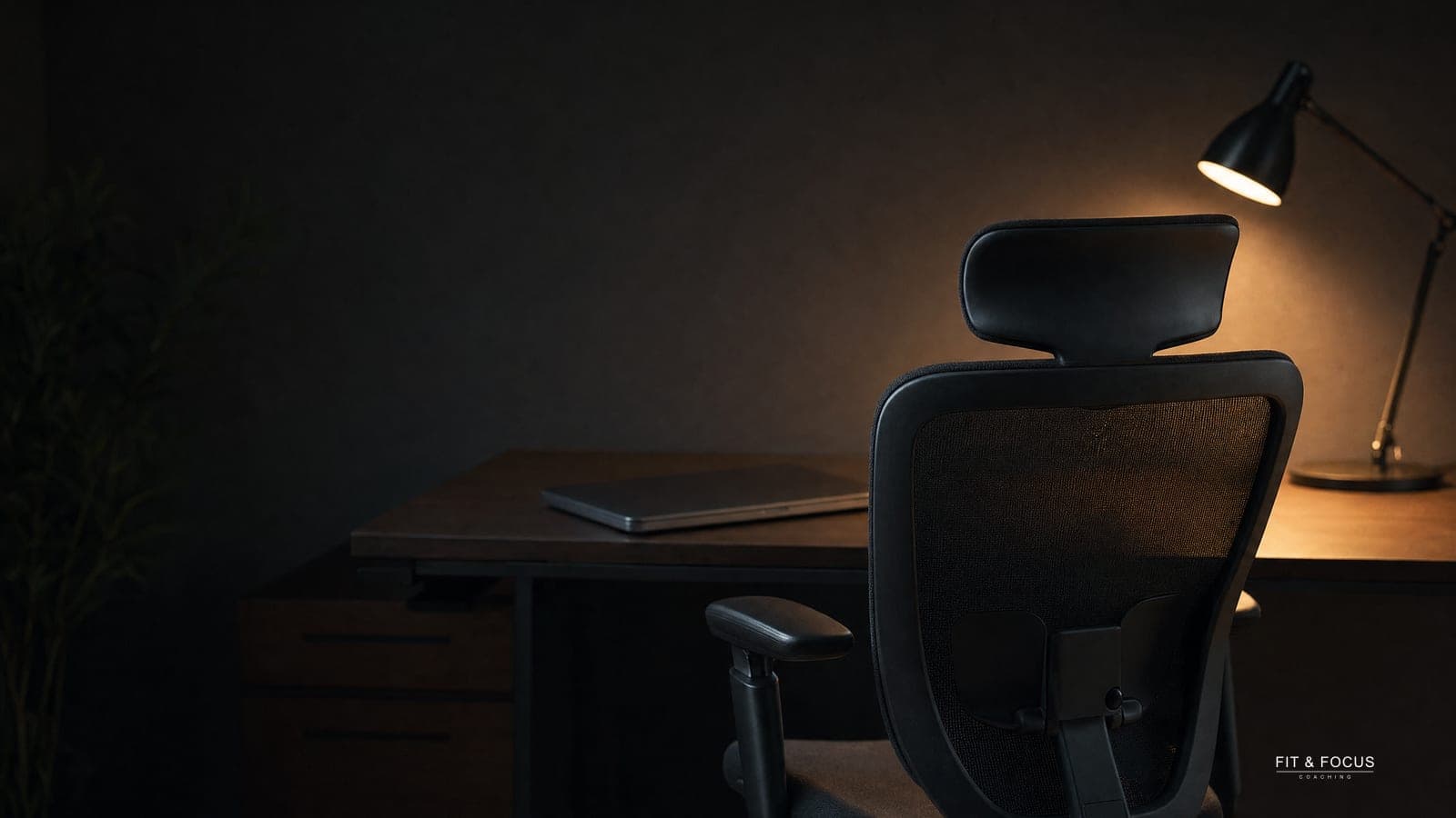 Lege bureaustoel bij een donker bureau met een gedoofde laptop