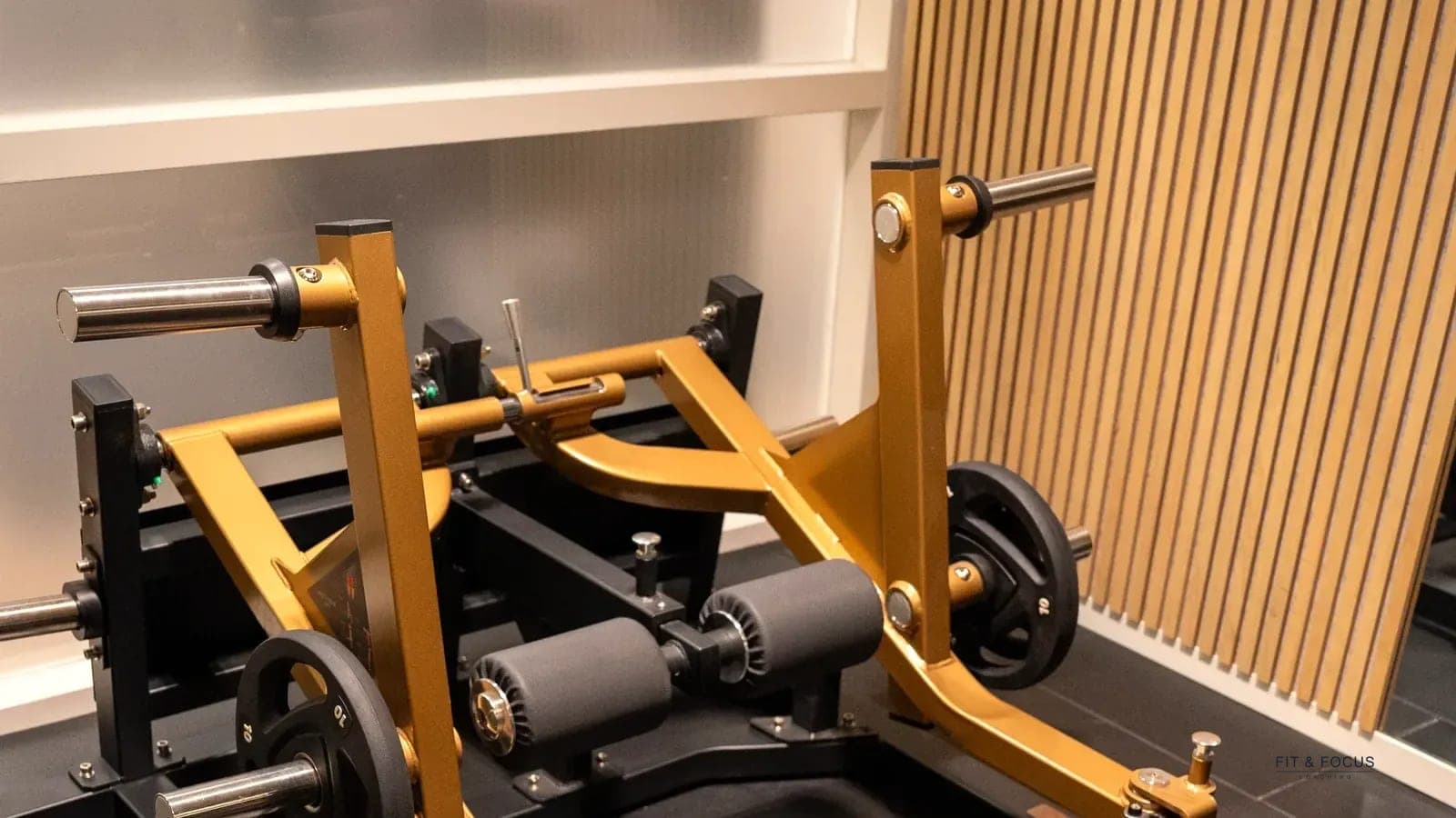 Squatmachine met goudkleurig frame tegen de houten lattenwand