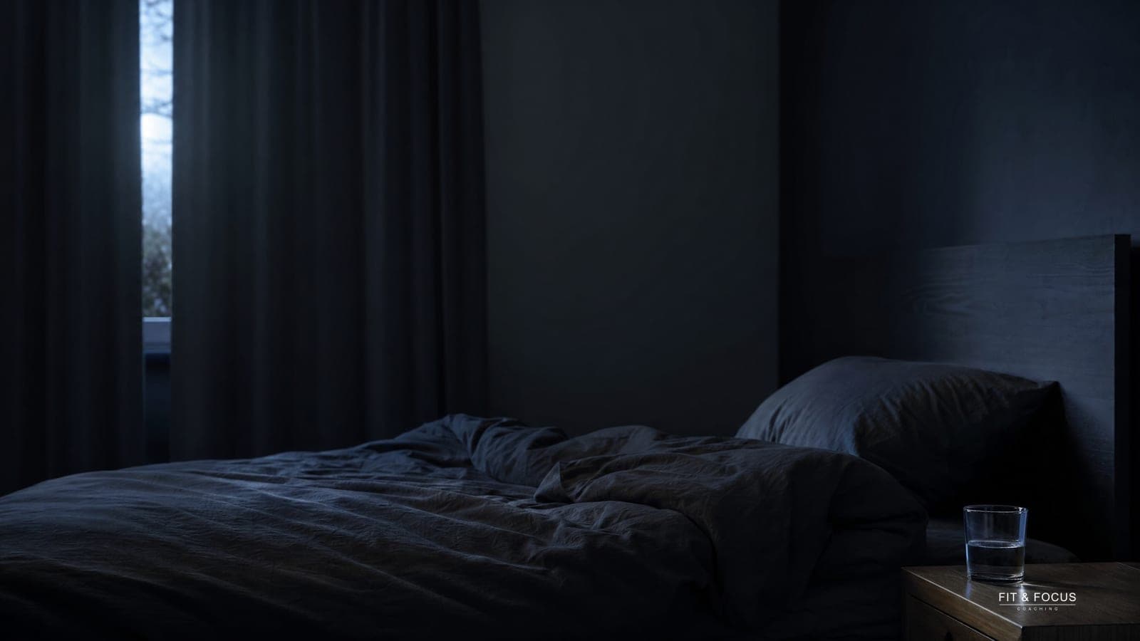 Onopgemaakt bed in een donkere slaapkamer met een glas water ernaast