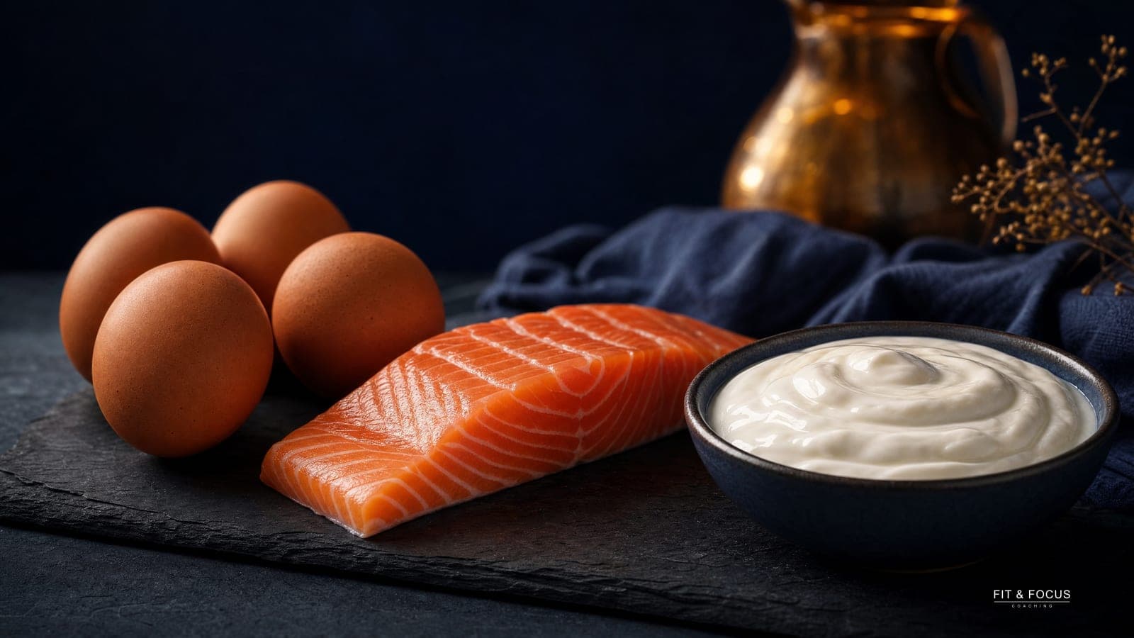 Verse eieren, een zalmfilet en een kom Griekse yoghurt op donkere leisteen